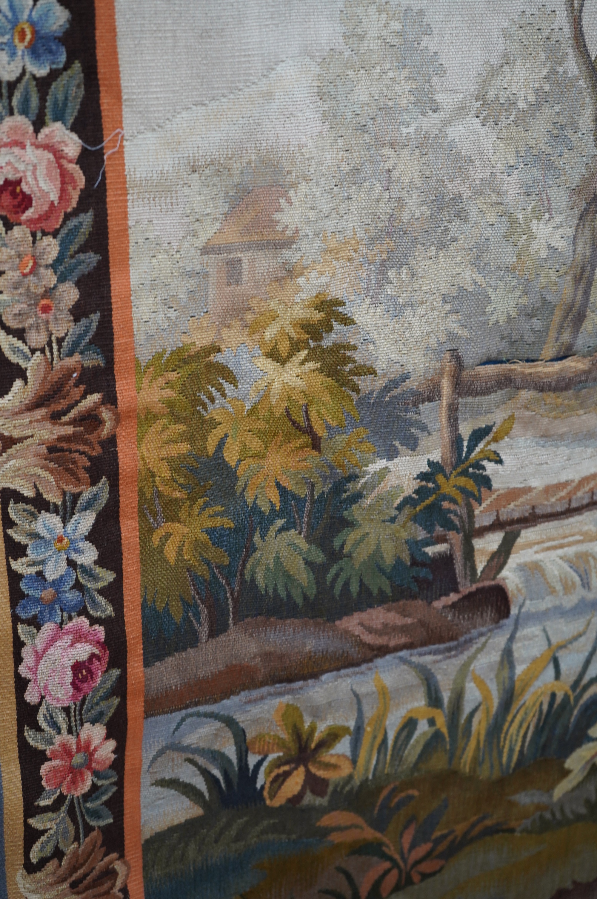 A 20th Aubusson wall hanging of a young man and lady fishing in a river in the foreground with a wooden bridge, house and chateau in the background, 169 cm wide, 122 cm high. Condition - good